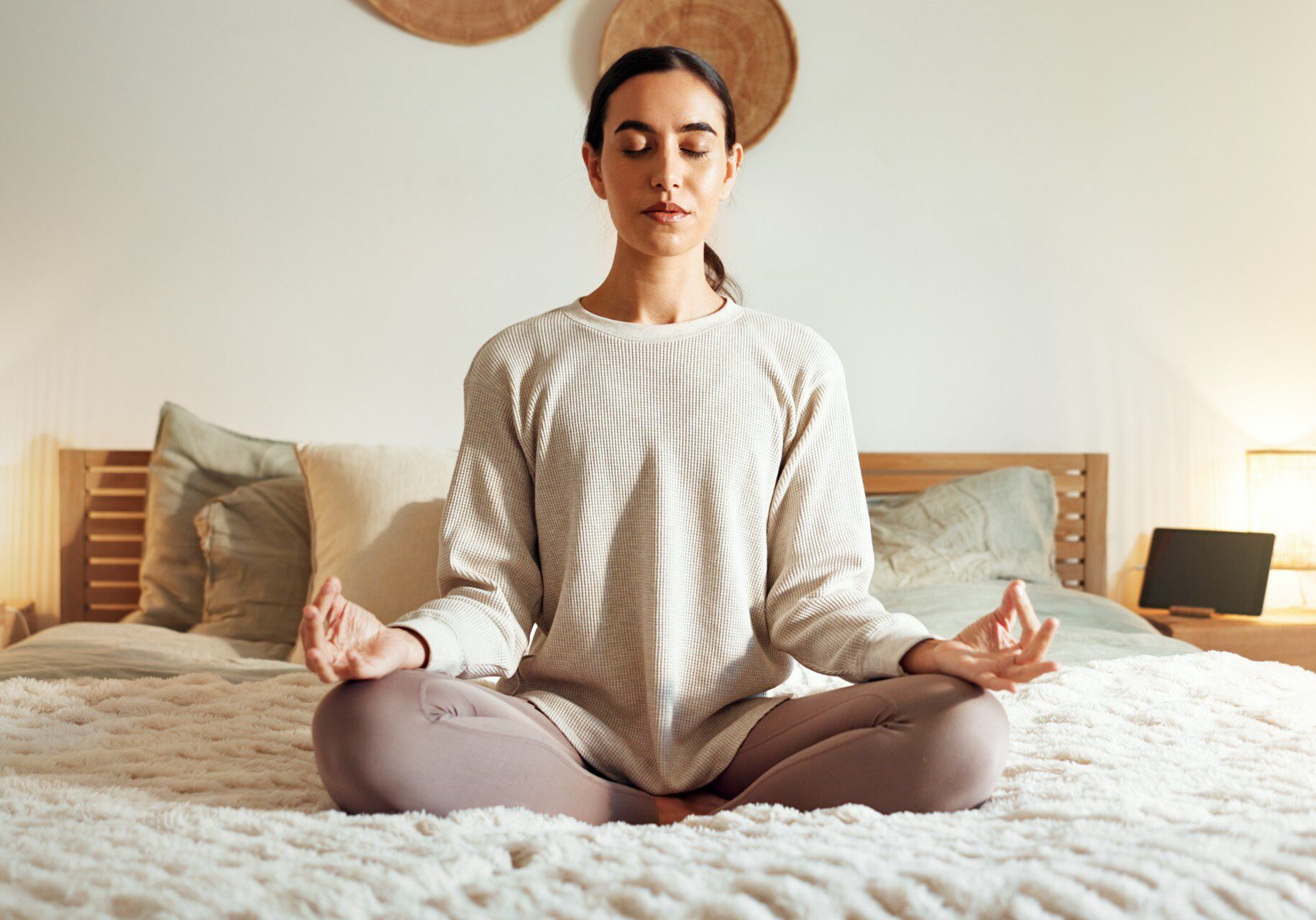 Woman meditating on bed, eyes closed.